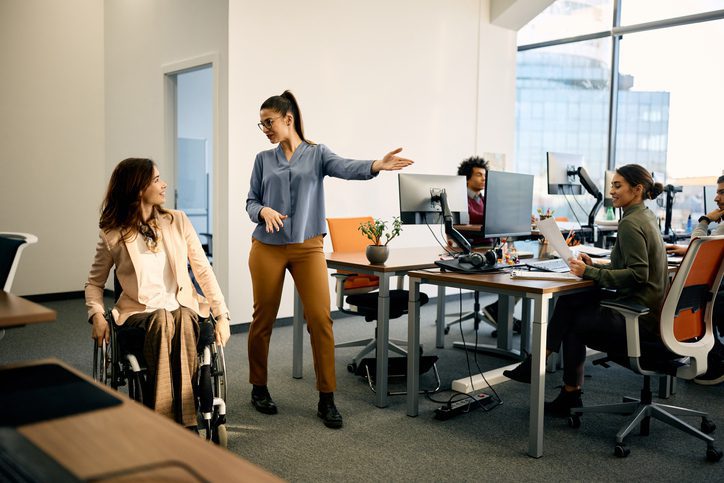 Happy businesswoman talking to her disabled colleague while leading her through the office